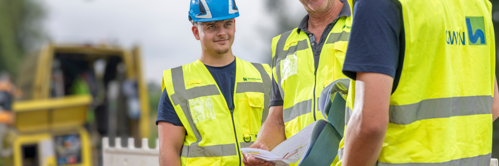 Drei Männer in Arbeitskleidung der GELSENWASSER Energienetze stehen an einer Gas-Baustalle und  unterhalten sich.