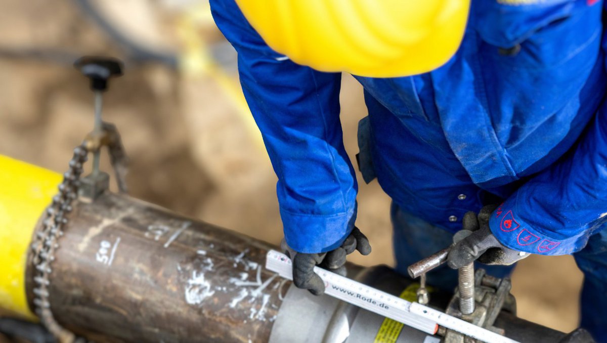 Ein Arbeiter beugt sich über eine Gasleitung in einer Baugrube.